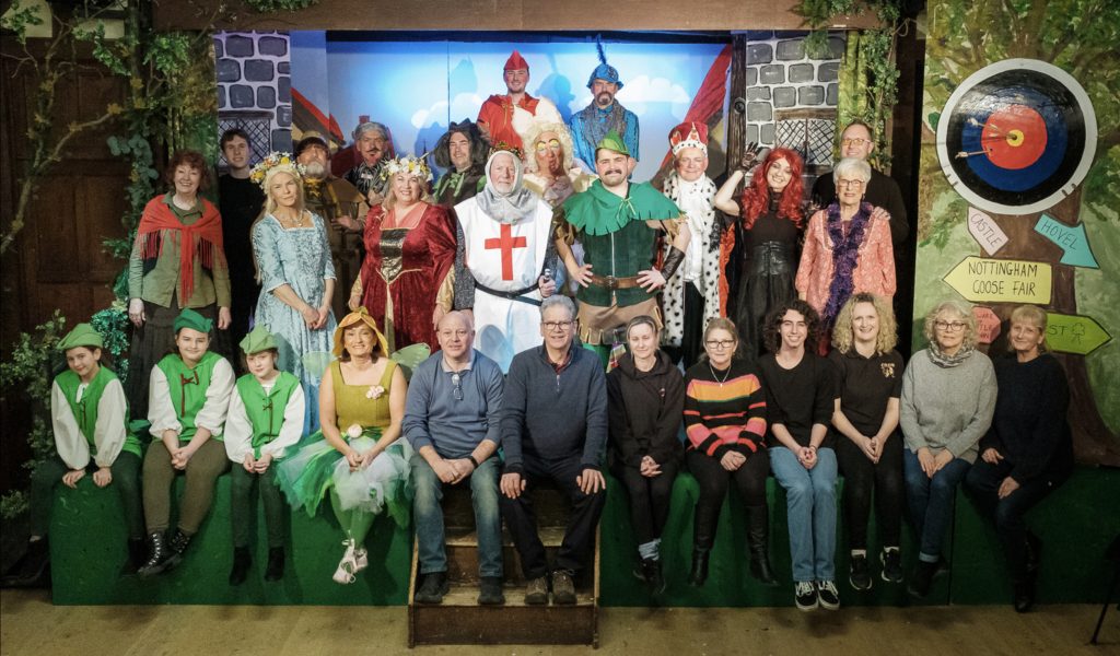 The full company pose for a group photos on stage, some in Robin Hood costumes.